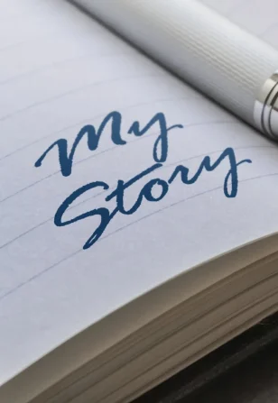 fountain pen resting on an open notebook with handwritten words My Story